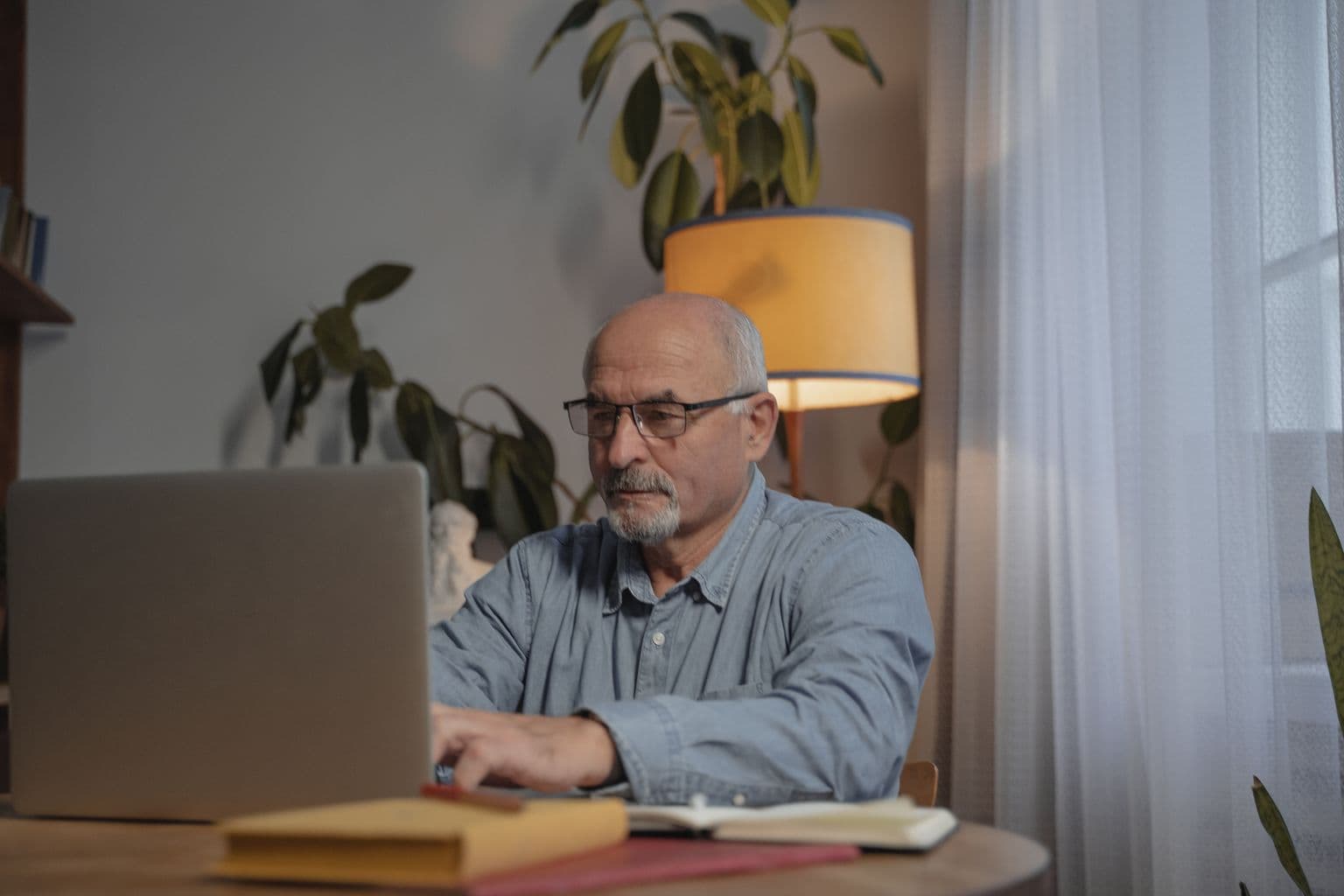 An older man wearing glasses and using a laptop at home.